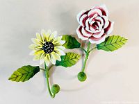 Photo showing both metal floral wall hooks, rose and daisy, on a white background to display design and details.