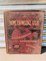 Front cover showing red cloth with gilt title 'Home Knowledge Atlas' and globe illustration