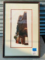 Frontal view of framed print showing beige and red double mat and black wood frame with gold accent