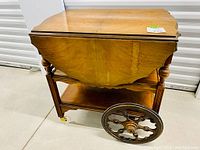Side angle view of solid maple tea trolley with one drop leaf lowered, showcasing wheels and leg details
