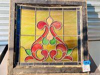 Front view of stained glass window showing the full design with yellow background and red, green, orange decorative elements in an old wooden frame.