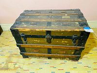 Front view of the antique steamer trunk showing latch and metal bands.