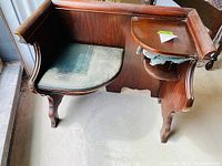 Front view of darkwood telephone table showing upholstered seat and small side shelf with visible wear and tear.