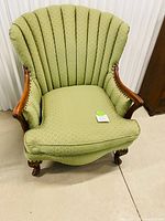 Front view of the antique wingback chair showing green upholstery and wooden arms with carved details.