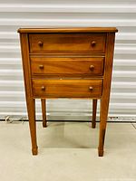 Front view of the wooden sewing cabinet showing three drawers with wooden knobs and tapered legs.