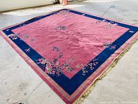 Main overview of rectangular wool area rug laid flat showing pink field, navy border and gold fringe