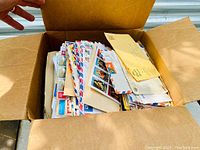 Open cardboard box showing a pile of assorted postal covers and envelopes, many with blue and red airmail borders.