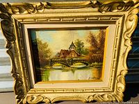 Framed oil on canvas painting featuring a village landscape with a stone bridge over a river, signed Bradley.