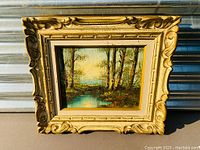 Frontal view of the framed oil painting showing the natural landscape scene and decorative frame.