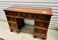 View of the full antique mahogany desk showing seven drawers, bun feet, and brass hardware on a light concrete floor.