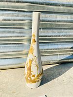 Full view of tall slender white porcelain vase with gold figure and floral designs.