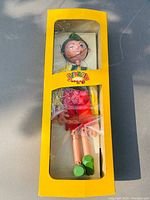 Photo showing the vintage Pelham Pinocchio marionette puppet inside its original yellow box with plastic windows.