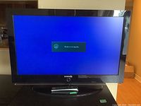 Samsung TV turned on with 'Weak or no signal' message on screen, showing unit powers on. Remote placed in front of TV stand.