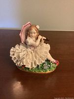 Front view showing the figurine's seated pose, parasol, and flute in hands, detailed lace dress and floral base.