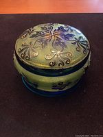 Front view of green glass lidded bowl showing floral hand painted design on lid and base with minor imperfections in glass surface.