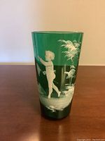 Front view of green glass cup with hand painted white child figure reaching up.