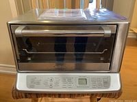 Full front view of Cuisinart stainless steel toaster oven on a wooden chair, showing glass door and stainless handle.