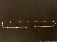 Full view of elegant gold chain necklace with oval pink coral inlays spaced along its length on a black background