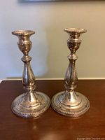 Pair of sterling silver candlesticks standing upright on wooden surface showing front view and base details.