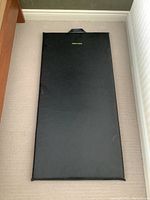 Photo of black exercise floor mat laid flat on carpeted floor, showing overall length and width with carry handle at top.