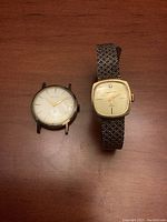 Two vintage men's watches on wooden surface, left Bulova without band, right Waltham with textured metal band