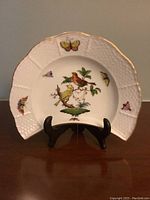 Front view of the Herend dish with bird and butterfly decoration on wooden stand.