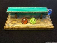 Side view showing handmade glass kaleidoscope with green body and blue end, mounted on a wooden base with two colored glass marbles in front.