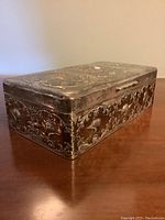 Closed box resting on wood surface, showing embossed side and lid details