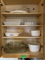 Photo of kitchen cabinet shelf showing white ceramic bakeware and metal tongs.