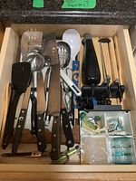 Drawer with assorted kitchen utensils and knives including spatulas, ladles, peelers, and more.