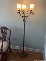 Full view of the floor lamp standing in room next to chair, showing three lights turned on.