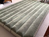 Full view of inflated green inflatable air bed on carpeted floor with visible horizontal ridges
