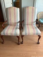 Front view of two upholstered captain chairs with striped fabric and solid wood frames.