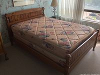Double bed with floral-patterned Serta mattress on solid wood frame showing headboard and footboard with turned posts.
