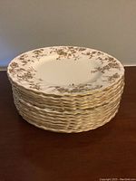 Stack of 12 identical Minton salad plates showing scalloped gold edges and floral gold pattern on white ceramic.