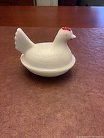 Front view of the white milk glass hen covered dish sitting on a wooden surface.