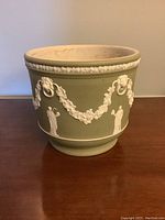 Overview of the green Wedgwood jasperware pot with white relief decorations, showing the front and part of the rim.