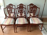 Front view of all six solid wood Hepplewhite style shield back dining chairs with multicolored upholstered seats, arranged in two rows of three.