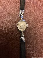 Front view of the vintage ladies watch with silver-tone dial and black leather band.