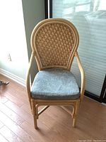 Wicker chair with woven backrest and armrests, padded seat cushion with palm tree print shown from an angle.