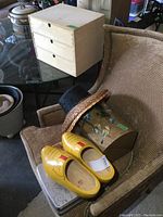 Wooden dome top chest with floral painting, pair of yellow painted wooden clogs, two sun hats (straw and black), and tins on chair