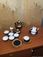 Full set displayed on wooden table showing teapot, creamer, sugar bowl, six demitasse cups with saucers, and separate Coalport teacup with saucer.