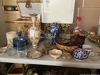 Wide view showing tall blue and white vase, decorative bowls, small baskets, vanity box, glass elephant, and various glassware on table.