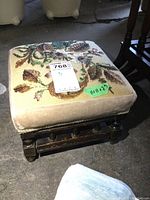 Top front view of an upholstered wood footstool with floral tapestry.