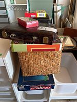 Lot items stacked including Monopoly box, woven basket, art case, backgammon case, cards kits for Bartender's Deck and I Ching cards