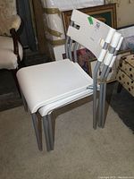 Three white plastic chairs with silver metal frames stacked together, showing design and condition.