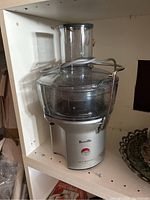 Breville Juice Fountain juicer placed on a white shelf, showing the full unit and the juice container details.