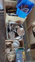 Photo showing three boxes filled with various kitchen items including cookware, a French press, metal rack, and storage containers.
