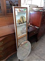 Tall rectangular mirror standing against furniture shows wear on frame.