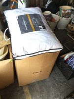 Box containing multiple bed pillows, some new in plastic packaging, along with other items around it.